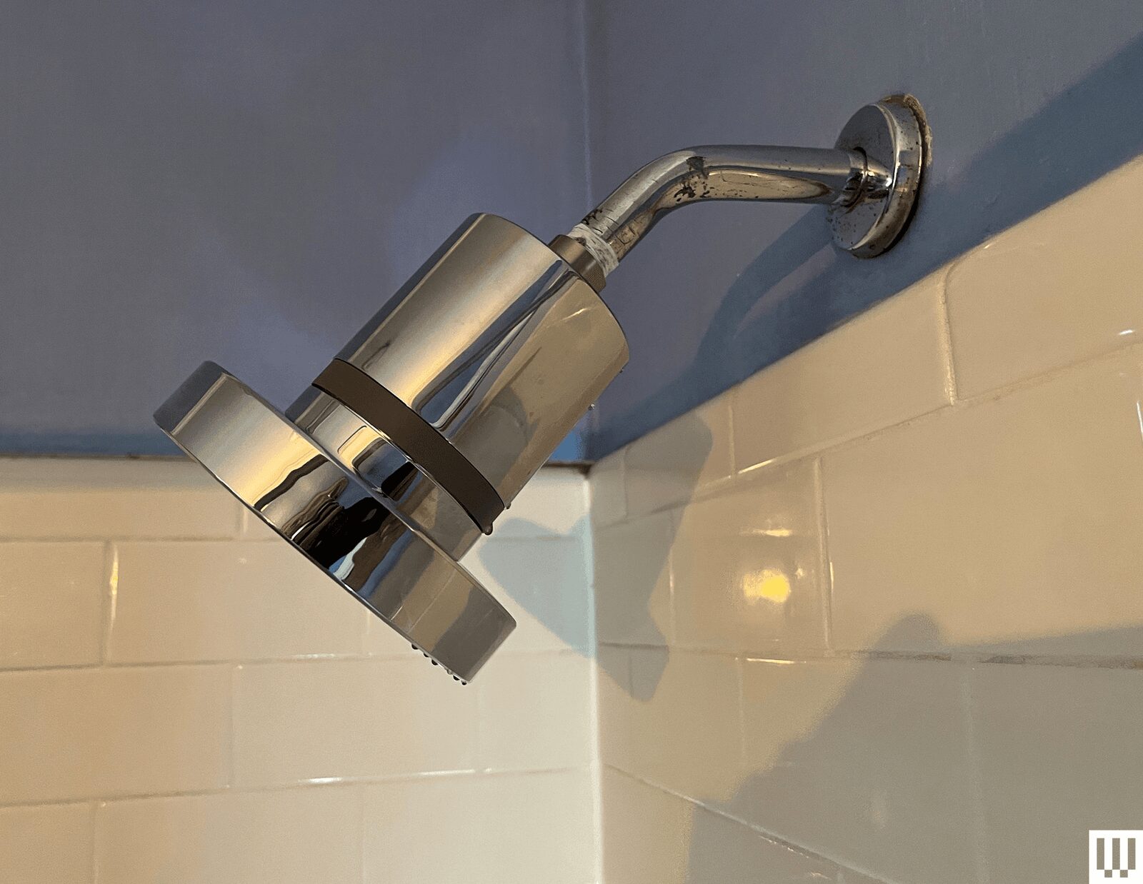 Silver showerhead with white tiles and blue walls in the background
