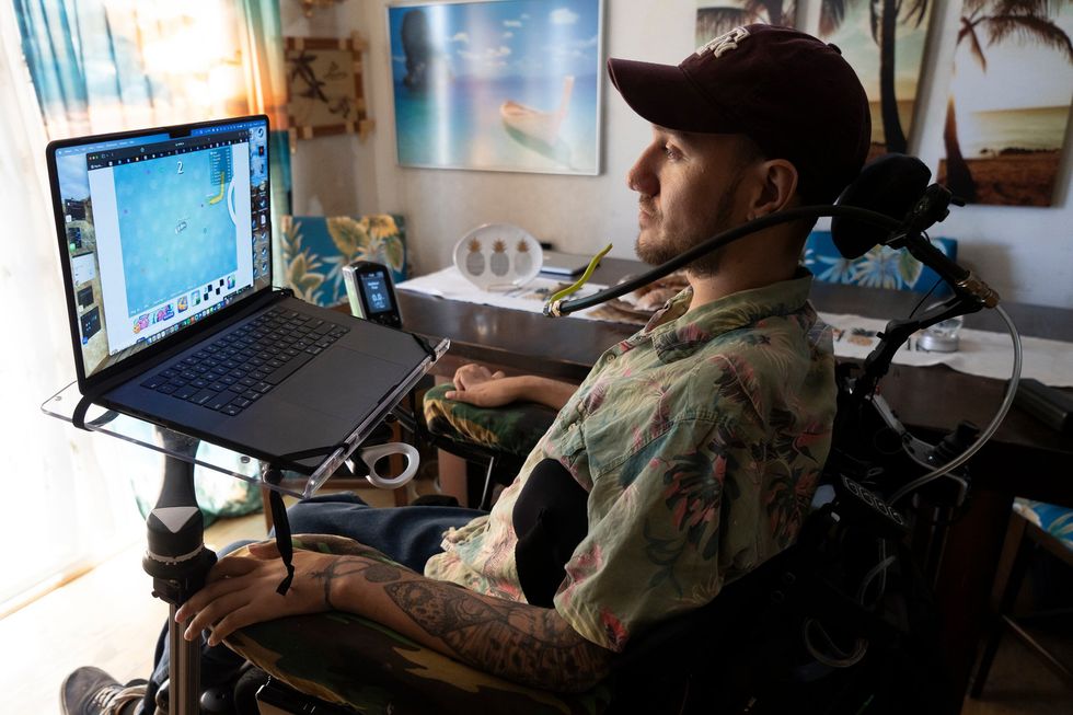 A man seated in a wheelchair looks at the screen of a laptop thatu2019s mounted on his wheelchair.