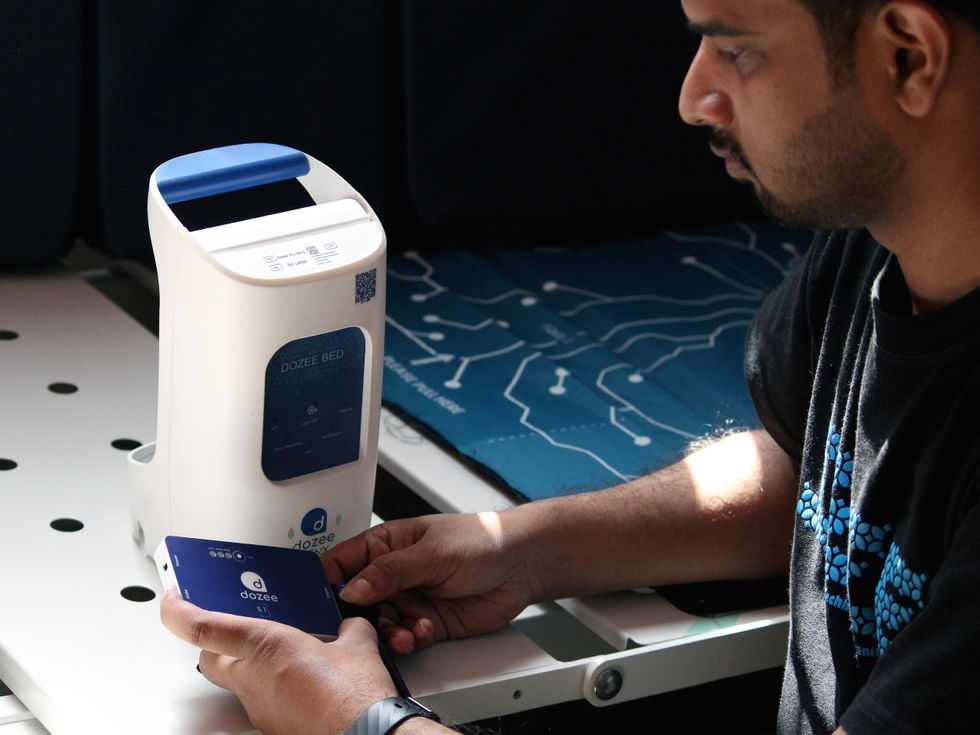 An adult Indian man looking at a rectangular device in his hand, labeled u201cdozeeu201d.