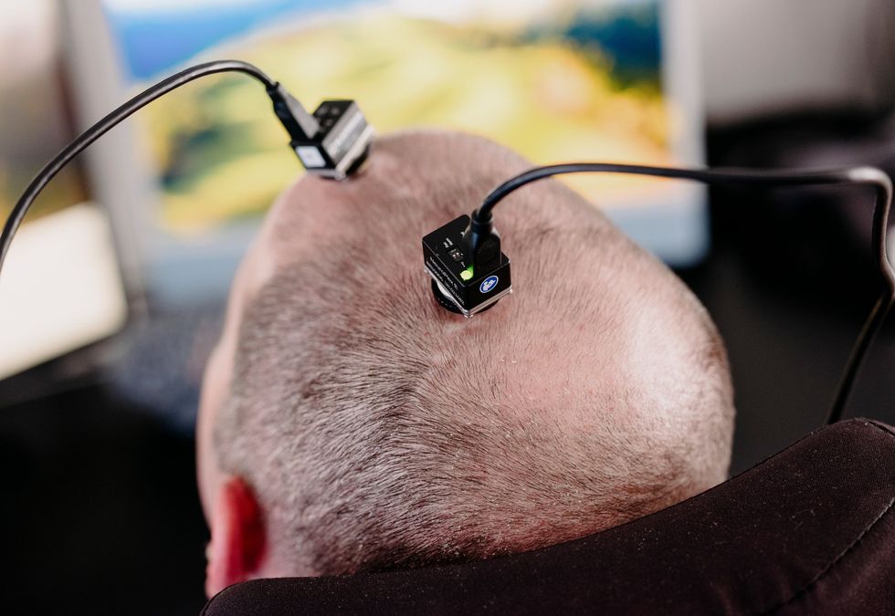 Bald head with wired brain-computer interface sensors attached in front of a monitor
