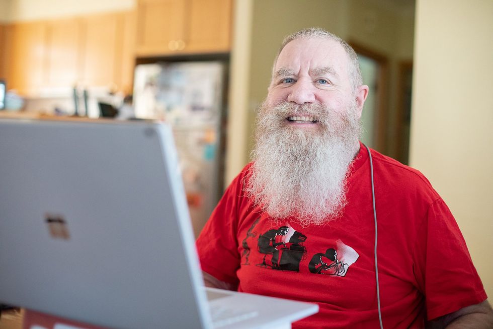 Bearded person in red Tu2011shirt using a laptop at a kitchen table