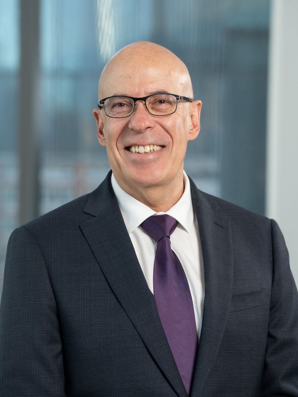 Businessperson in dark suit and purple tie standing in a modern office setting