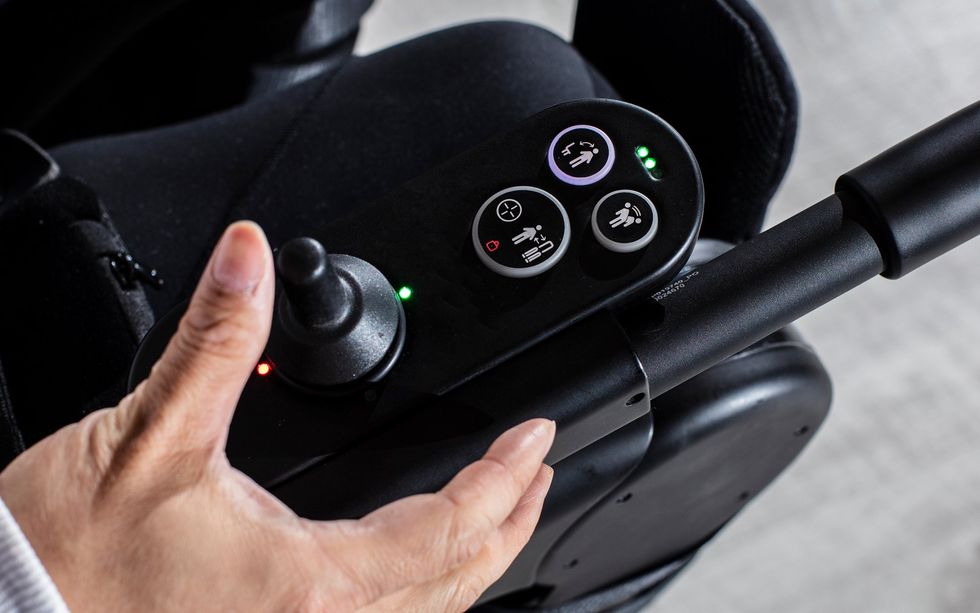 Close-up of a hand operating the joystick and controls on a powered wheelchair armrest