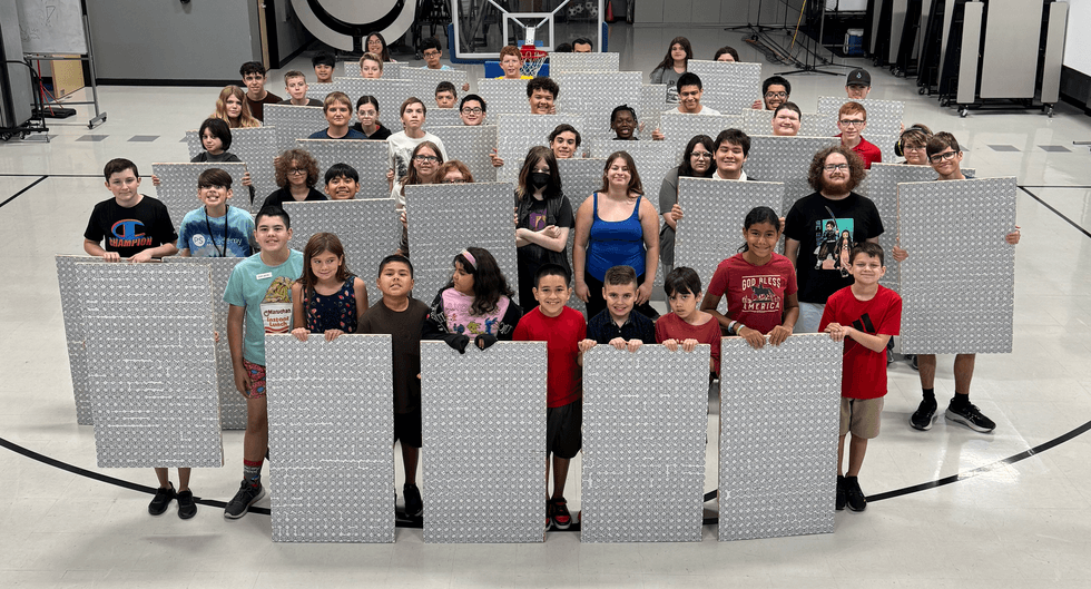 Group of students in a gym holding large silver patterned boards facing the camera.