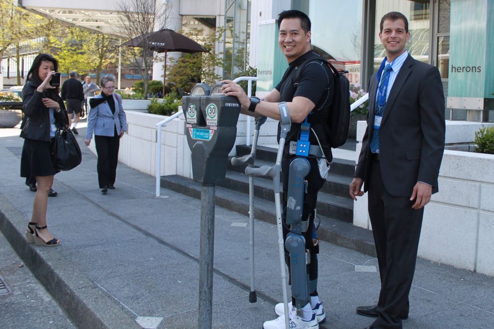 Man wearing robotic exoskeleton and using crutches on a city sidewalk