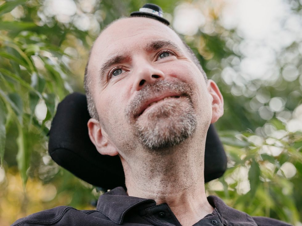 Person in a wheelchair outdoors, surrounded by green foliage and soft sunlight.