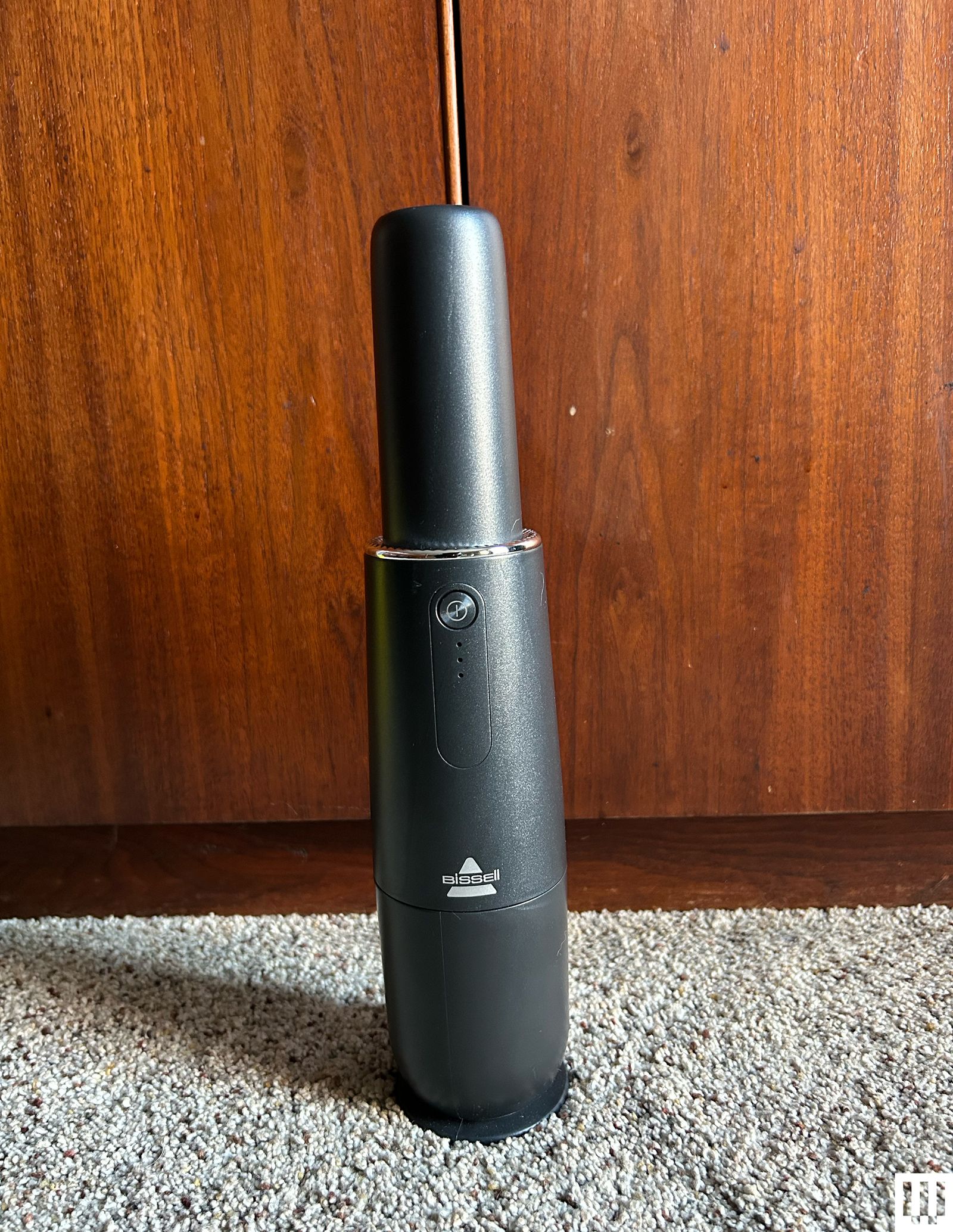 Bissell AeroSlim Handheld Vacuum propped up against a wooden panel with carpet underneath it