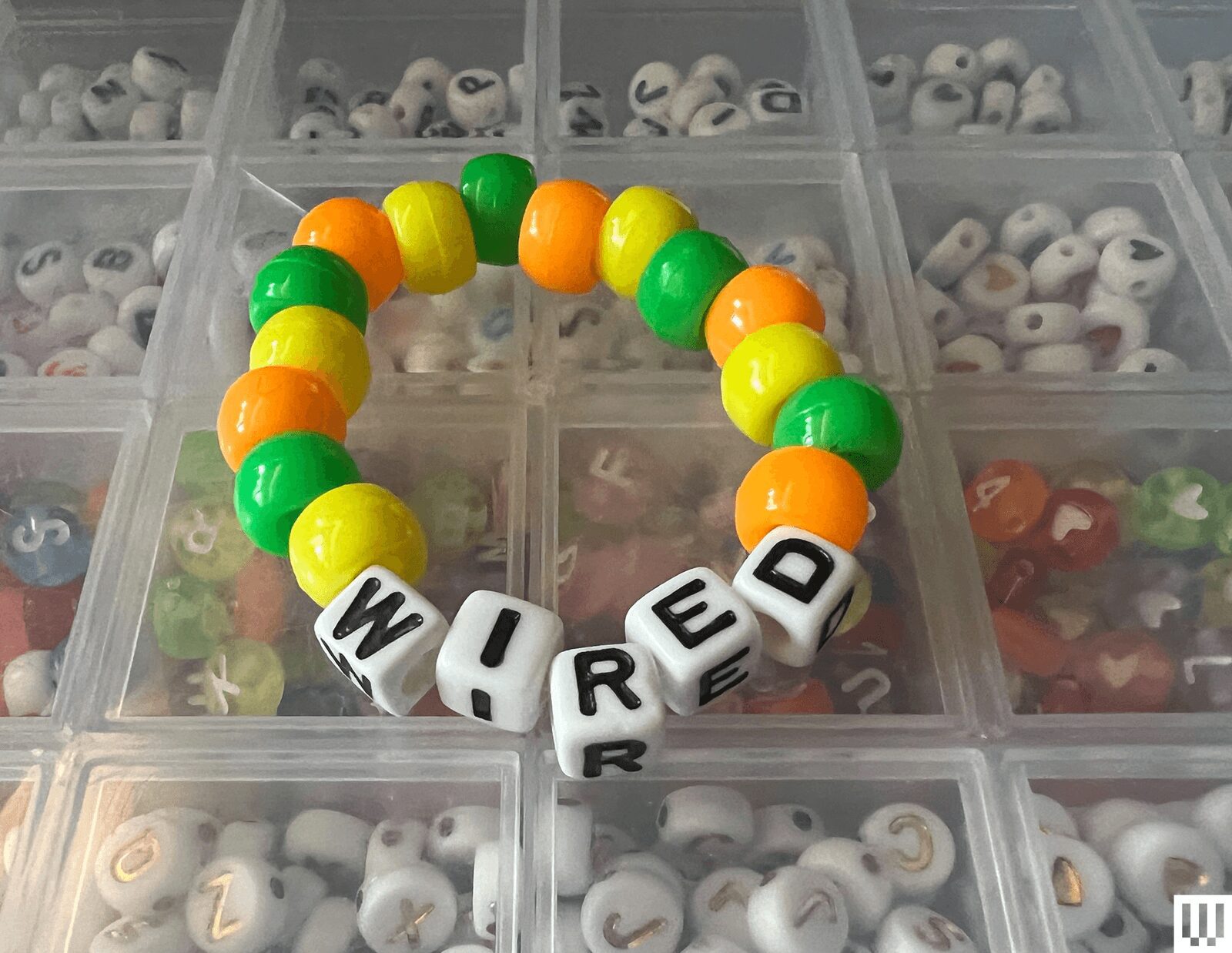 Beaded bracelet with orange yellow and green balls surrounding white block beads with letters that spell out wired....