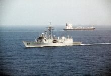 A tanker and a United States naval vessel passing through the Strait of Hormuz