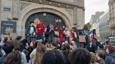 Students gather outside Lycée Jules Ferry in Paris with placards during a school protest.